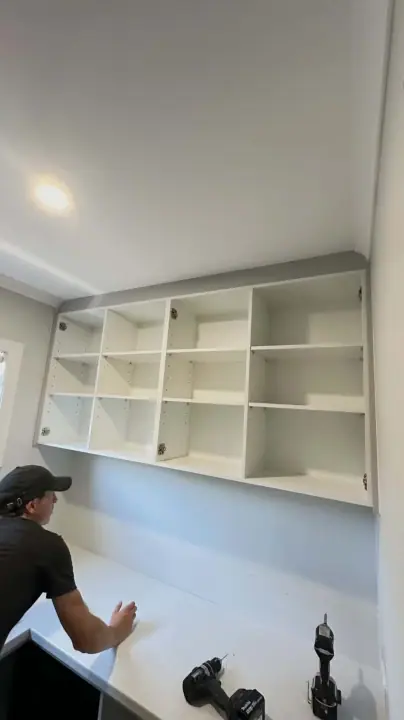 Installer fitting overhead pigeon-holes above a desk bench