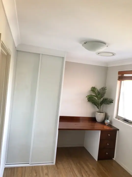 Timber desk beside white glass sliding wardrobe doors