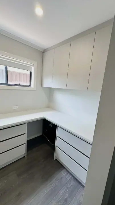 L-shaped built-in desk with drawers under a window and overhead cupboards