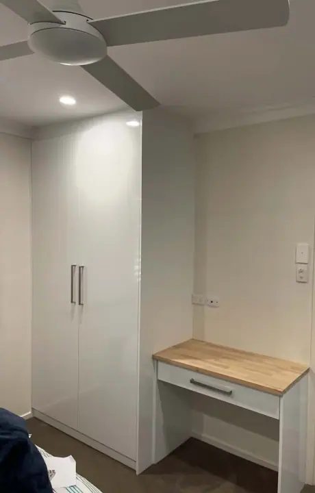 Tall hinged cupboard beside a timber-top study desk in a bedroom