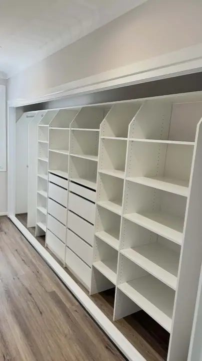 Long wardrobe internals with a drawer tower and adjustable shelving on timber floors