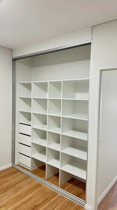 Sliding wardrobe open to a wall of pigeon-hole shelving and drawers