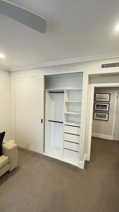 Sliding wardrobe open to show hanging, shelves and drawers in a living room