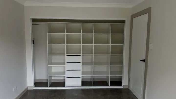 Wide sliding wardrobe with the doors open, showing shelving and a drawer bank