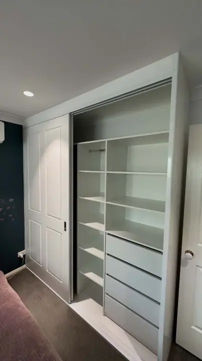 Sliding wardrobe internals with shelving and drawers against a navy wall