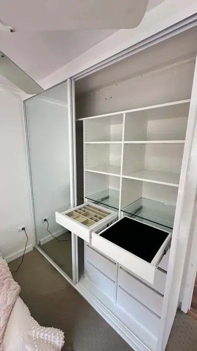 Mirrored sliding wardrobe open to a jewellery drawer and drawer bank
