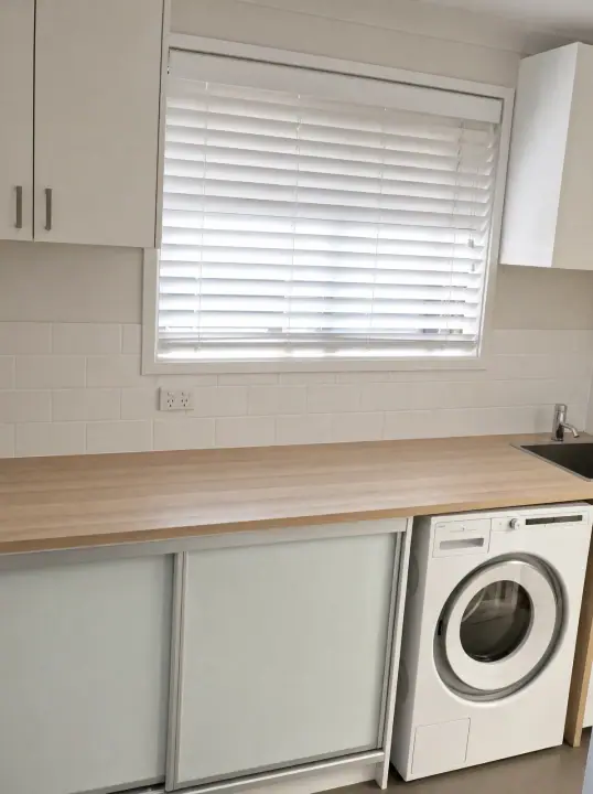 Laundry with a timber-look benchtop and sliding cupboards under the window