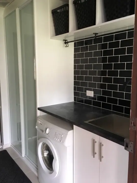 Laundry with black subway tiles and white base cupboards