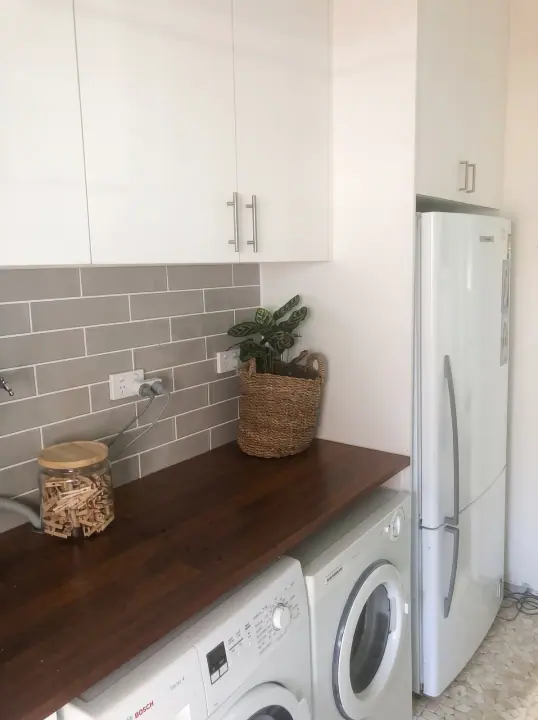 Laundry with white cupboards, timber benchtop and grey subway tiles