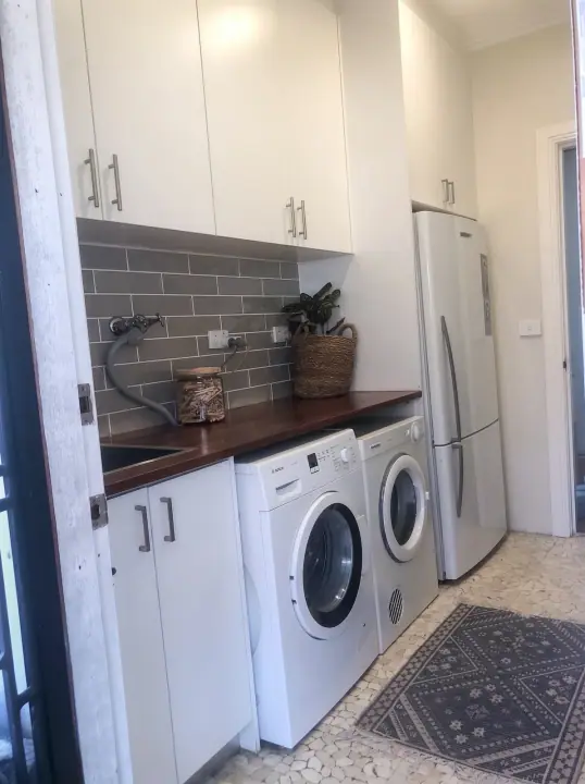 Laundry with white cabinetry, timber bench and fridge space