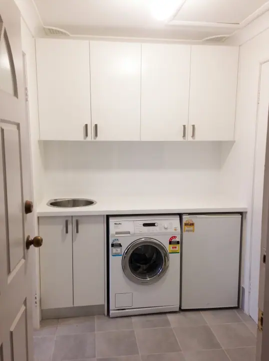 Laundry with overhead cupboards, bench and washer