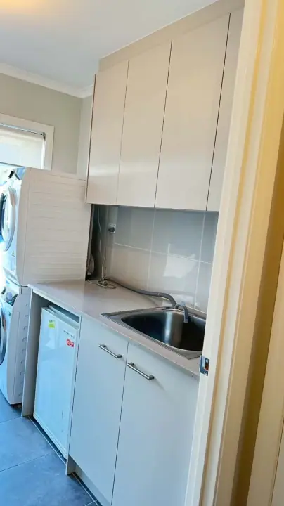 Compact laundry with white overheads, a sink and a front-loader under the bench