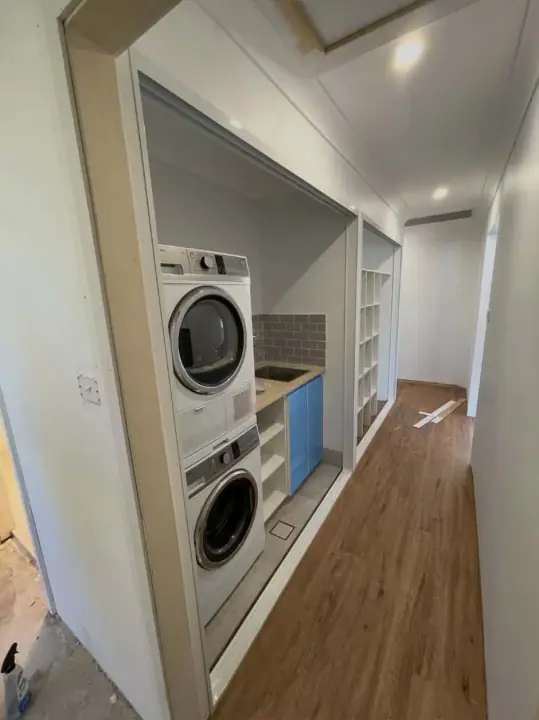 Stacked washer and dryer in a blue laundry cupboard off the hallway