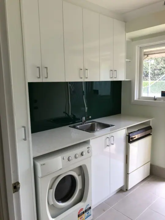 Laundry with white cupboards, dark splashback and a stainless sink