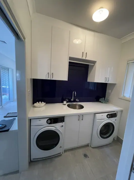 Laundry with a washer and dryer under a stone-look bench and navy splashback