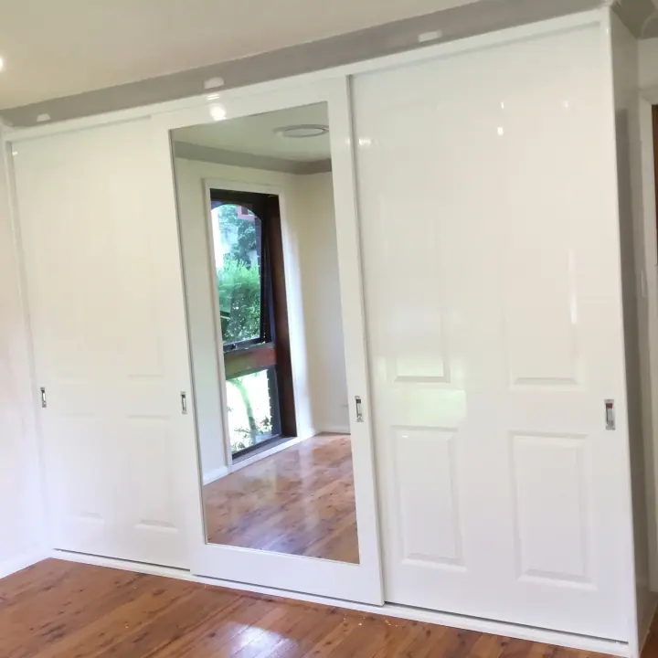 White panel sliding wardrobe with a full-height mirror door, opening onto a sunlit bedroom