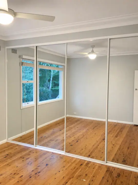 Three mirrored sliding doors reflecting polished timber floors