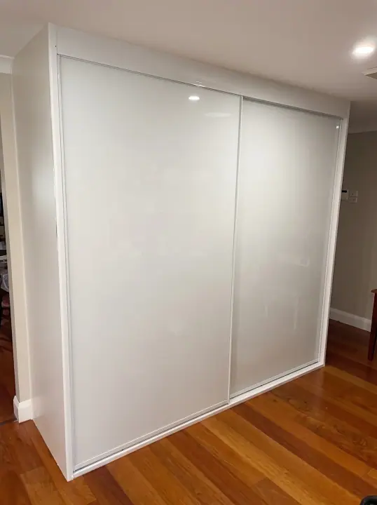 Two-door white glass sliding wardrobe beside a timber-floored hallway