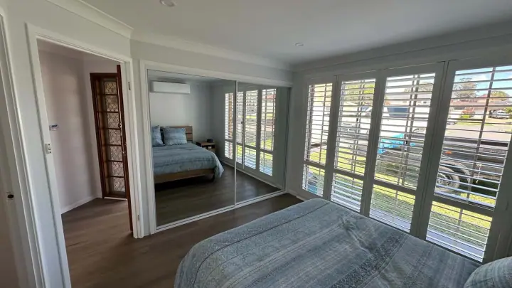 Three mirrored sliding doors reflecting plantation shutters and a bright bedroom