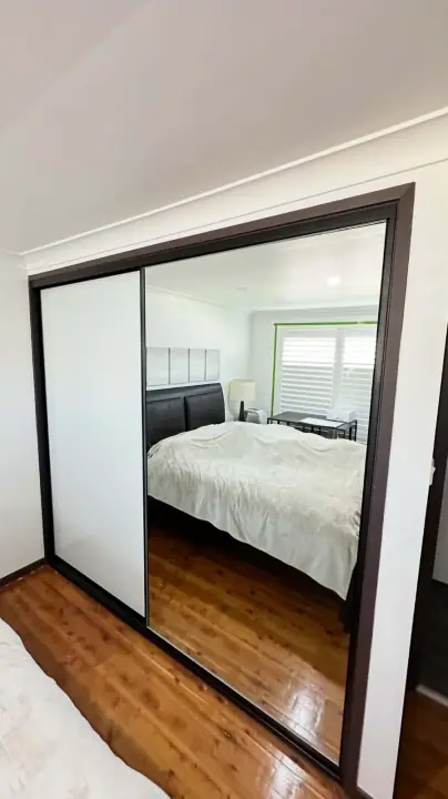Two mirrored sliding doors with a dark frame, reflecting a timber-floored bedroom