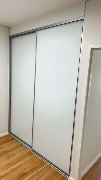 Two white glass sliding doors in a bedroom with timber floors