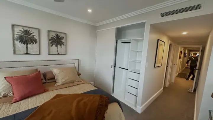 White sliding wardrobe open in a bedroom, showing hanging, shelving and drawers
