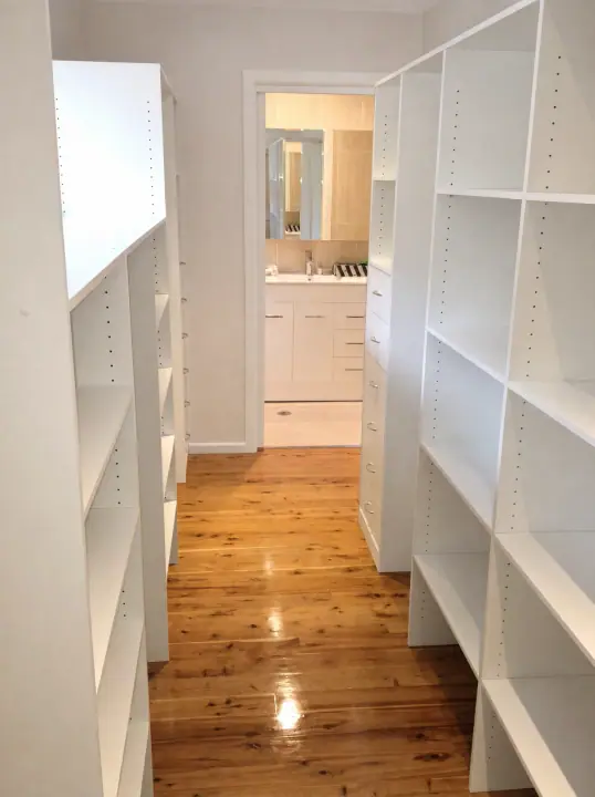 Walk-in wardrobe built around a window, with timber floors