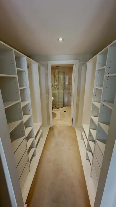 Narrow walk-in wardrobe with shelving both sides, leading through to an ensuite
