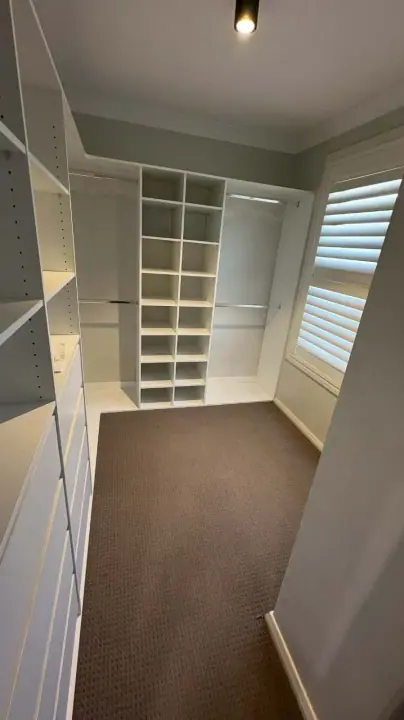 Walk-in wardrobe with shelving beside a window with plantation shutters