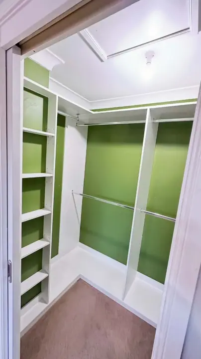 Small walk-in wardrobe fitted out against a green feature wall