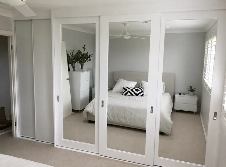 Mirrored sliding wardrobe doors reflecting a bright bedroom