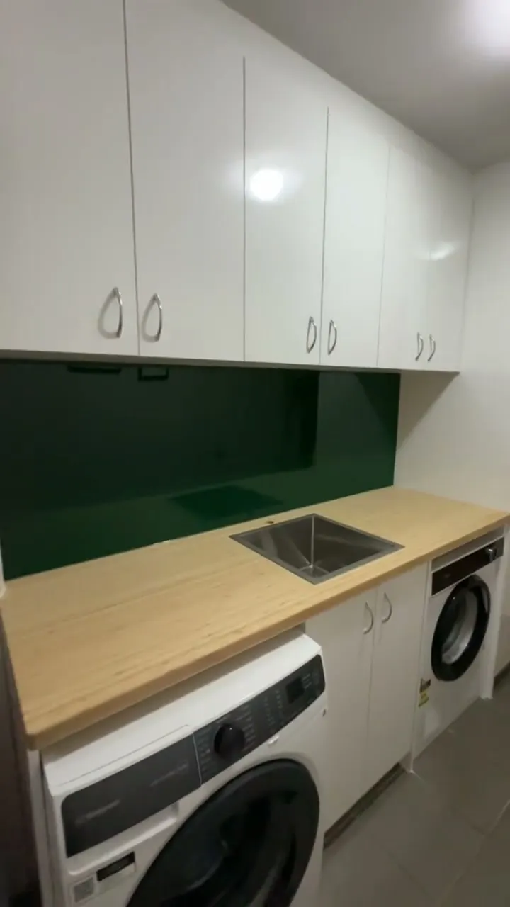Video: laundry with overhead cupboards, timber benchtop and a green splashback