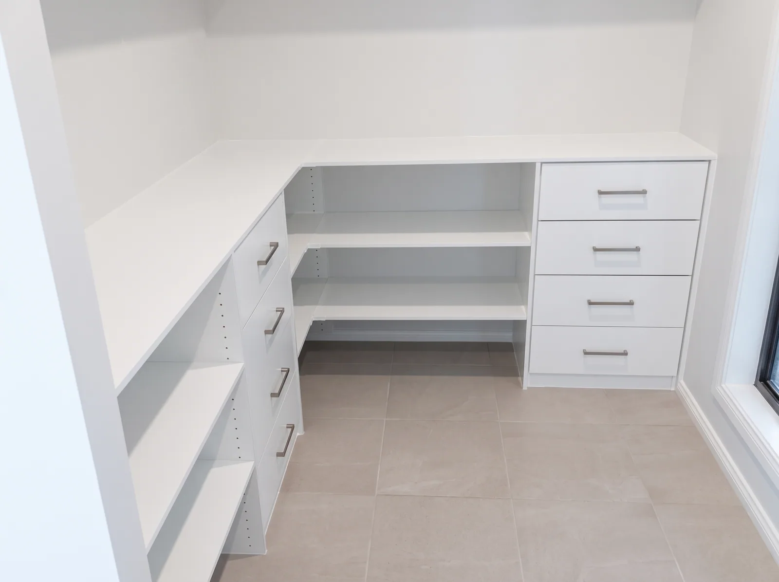 White L-shaped built-in desk wrapping a corner, with two drawer banks and open shelving beneath, built by Reflections
