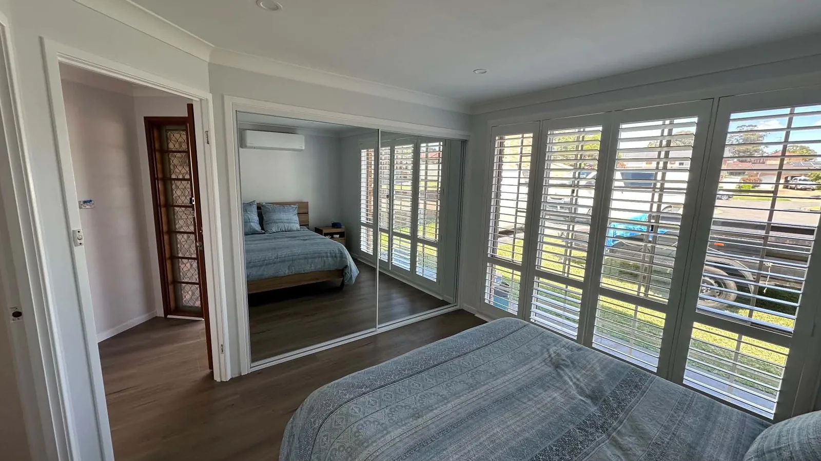 Three mirrored sliding wardrobe doors reflecting plantation shutters in a bright bedroom