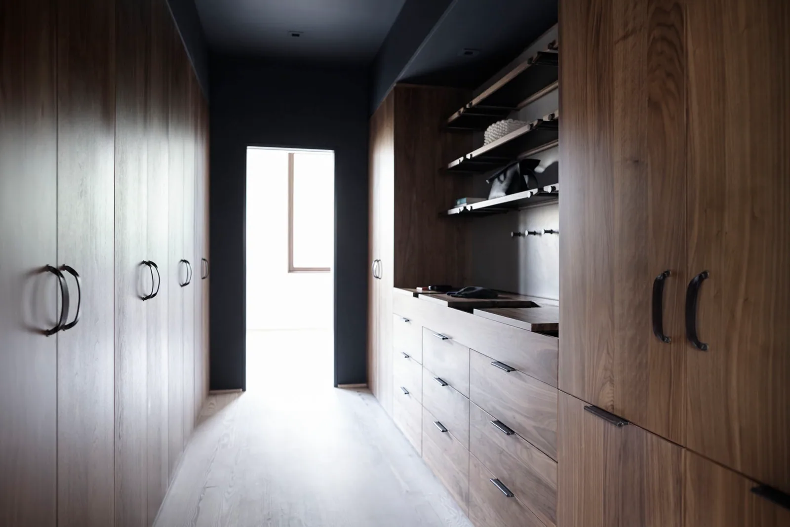 Long galley walk-in wardrobe lined with full-height woodgrain doors, a bank of drawers and open shelves, built by Reflections